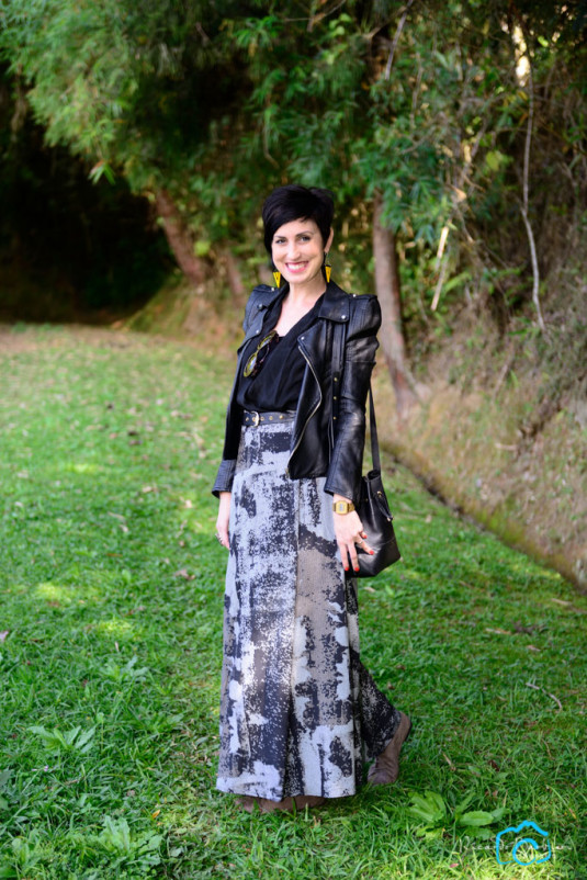 jaqueta com ombreiras de couro preta, saia longa com estampa em pixels preta, cinza e branca, bota cinza, macaquinho preto usado como blusa e com renda atrás, brincos amarelos