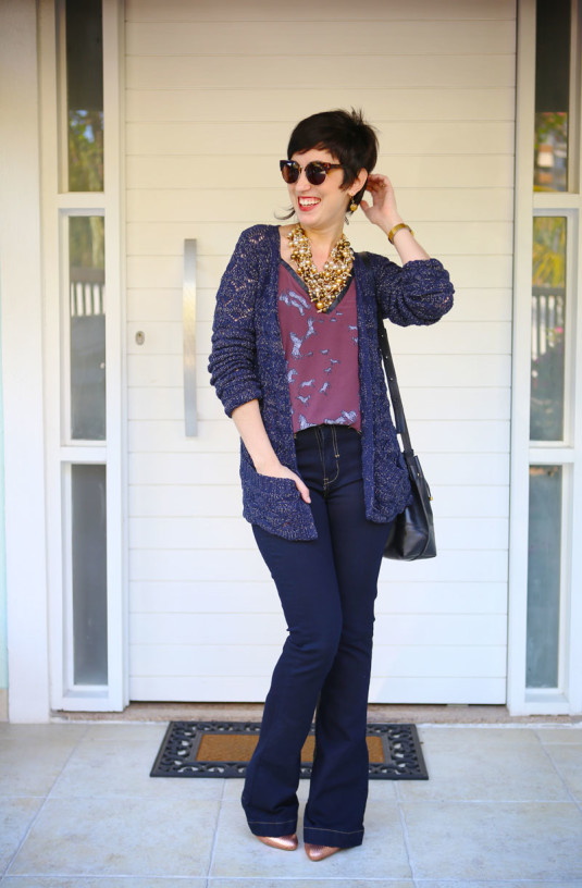 blusa vinho claro com estampa de zebras sem manga, tricô comprido azul escuro e fios dourados, calça jeans flare escura, scarpin dourado, bolsa saco preta