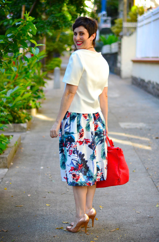 blusa branca neoprene manga curta, saia midi floral em azul, vermelho e verde, scarpin dourado, bolsa grande coral trançada, colar em pedras azuis e verdes