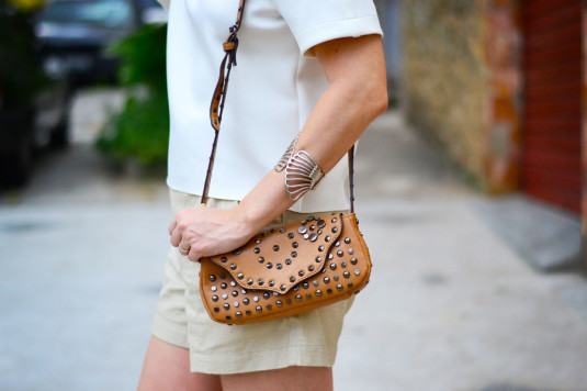 blusa branca com mangas curtas de neoprene, short de linho cru, colar prateado, sandália rasteira nude, bolsa pequena marrom com tachasas