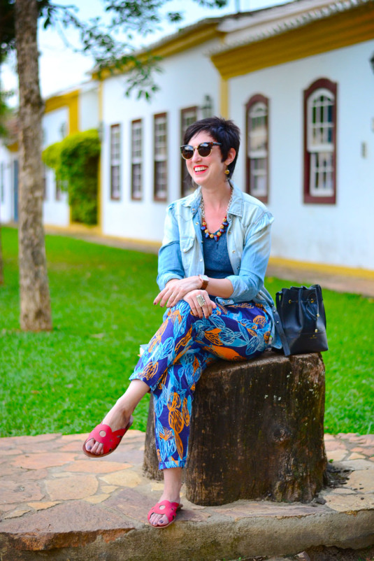 regata azul petróleo, calça com estampa de folas em azuis e laranja, camisa jeans clara, sandália de couro vermelha com círculos, colar vermelho, dourado e murano azul