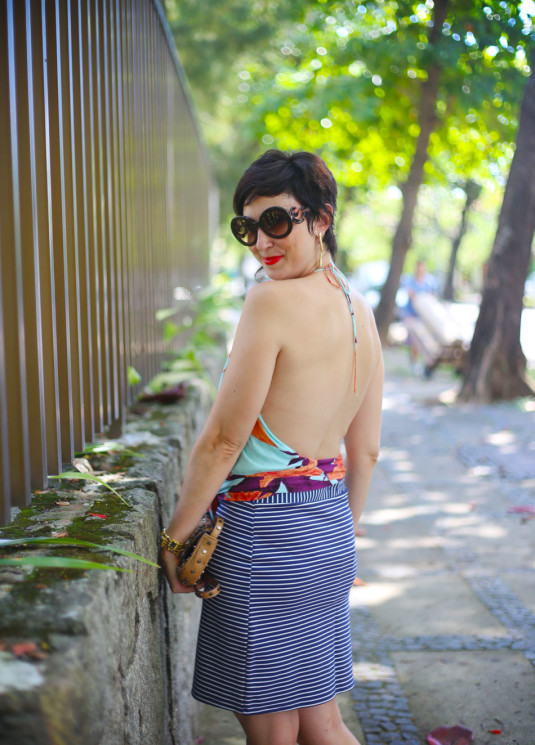 saia reta listrada mais ajustada, blusa frente única com estampa de flores laranjas, roxas, vermelhas e fundo azul claro, sapatilha bico fino dourada metalizada, bolsa pequena tiracolo bege de tachas