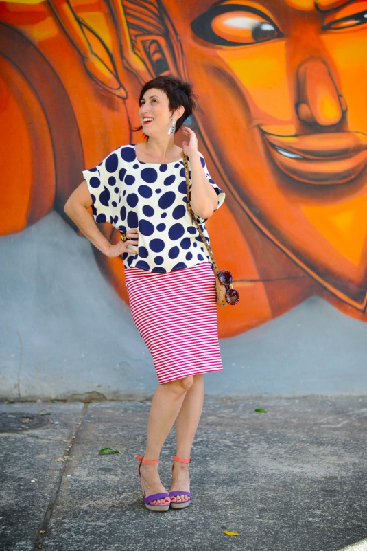 saia lápis de malha de listras vermelhas estreitas, blusa branca com bolas azul marinho de mangas curtas, sandália anabela laranja e roxa